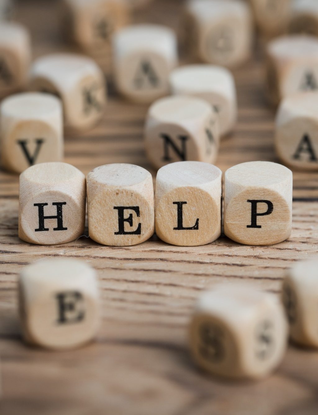 Hilfe zur Selbsthilfe Buchstabenwürfel zeigen das Wort "HELP" auf einem Holzuntergrund.